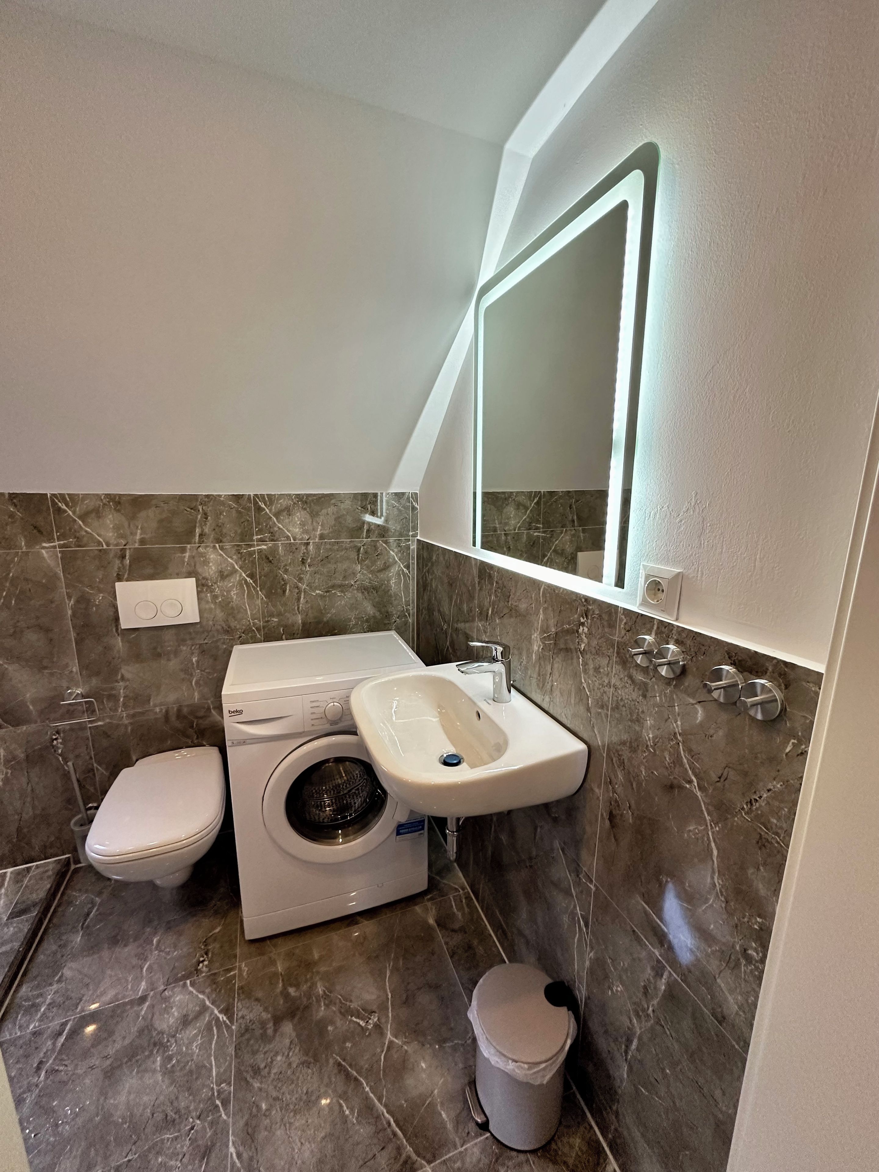Ein Badezimmer mit Waschmaschine, Waschbecken, Toilette und Mülleimer.