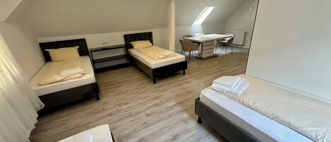 A modern hotel room with two single beds, a larger bed, a desk, and a chair.