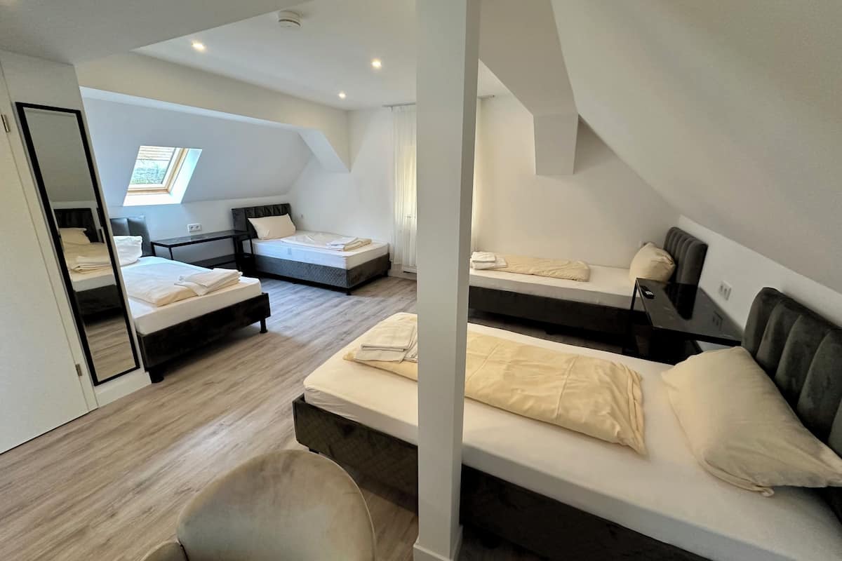A modern, well-lit attic bedroom with two beds, a desk, and a large mirror.
