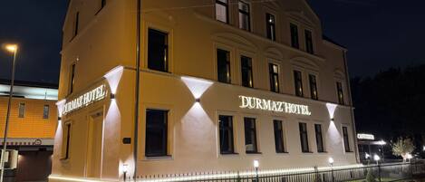 A hotel with a prominent sign, a well-lit facade, and a gated entrance.