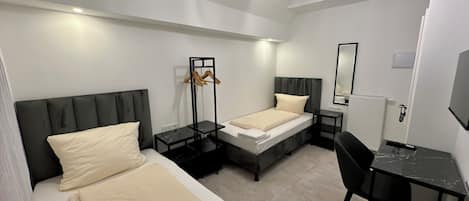 A hotel room with two beds, a desk, a chair, a mirror, and a hanging light fixture.