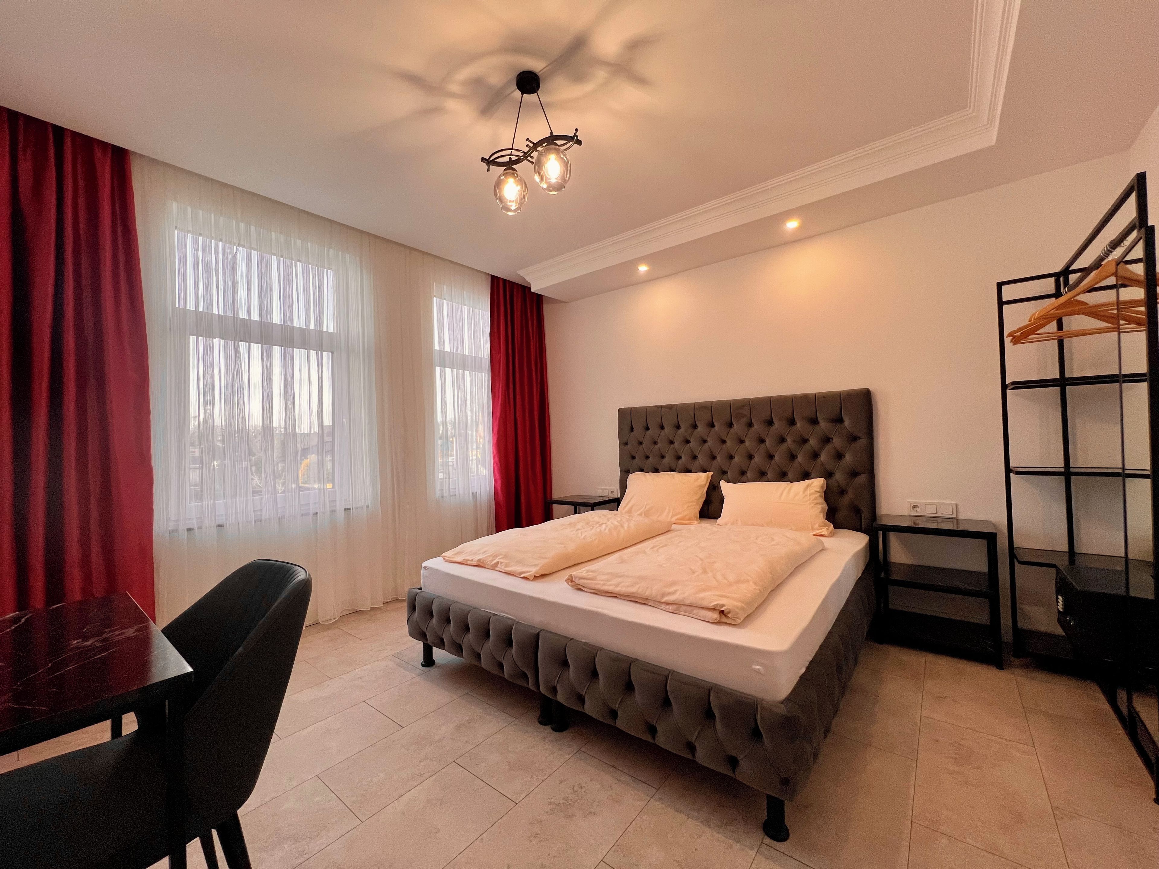 A neatly arranged bedroom with a tufted headboard bed, a small bedside table, and a hanging clothes rack.
