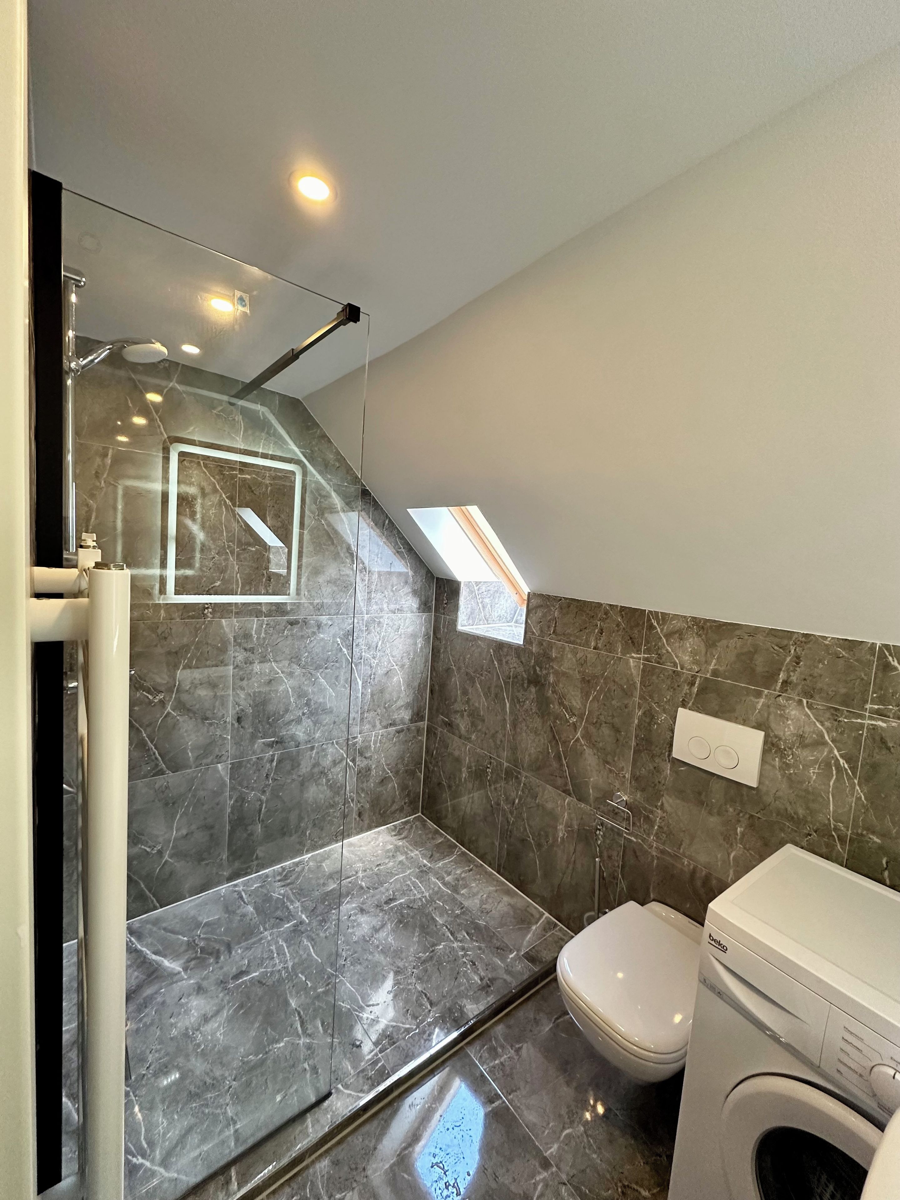 Ein modernes Badezimmer mit Dusche, Toilette und Waschmaschine.
