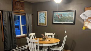 A dining area with a round wooden table, white chairs, a ceiling fan, and framed artwork on the walls.