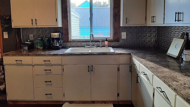 A kitchen with white cabinets, a granite countertop, a window with a view of a blue house, and a built-in sink.