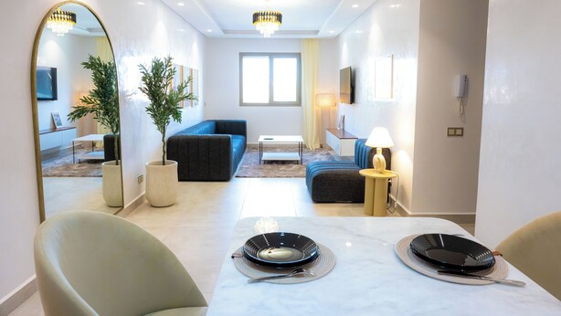 Un salon moderne avec un canapé, une table à manger dressée avec de l’assiette et un grand miroir.