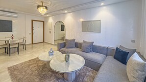 Un salon moderne avec un canapé, deux petites tables rondes, un lustre et un grand miroir.