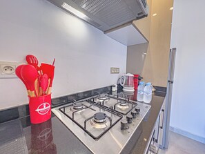 Una cocina moderna con estufa a gas, un recipiente rojo para utensilios y una tetera.