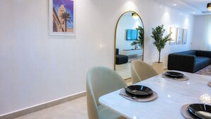 Un espace repas moderne avec une table en marbre, des chaises et un grand miroir. Un tableau encadré est accroché au mur, et une plante en pot est posée à proximité.