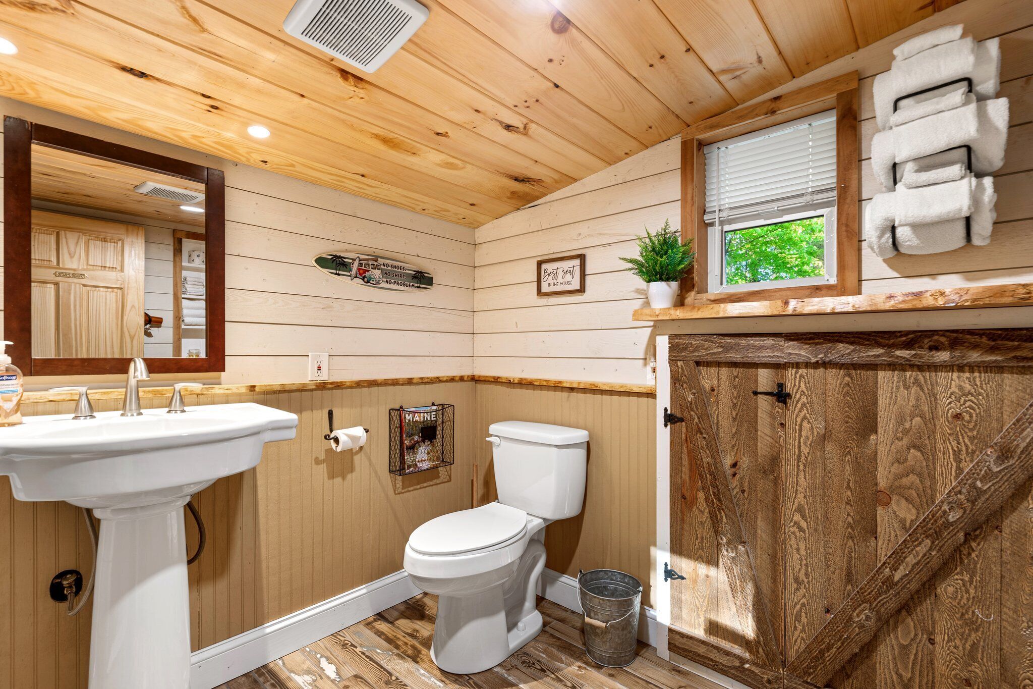 Une salle de bain aux murs lambrissés, équipée d’un lavabo, de toilettes et d’une fenêtre.