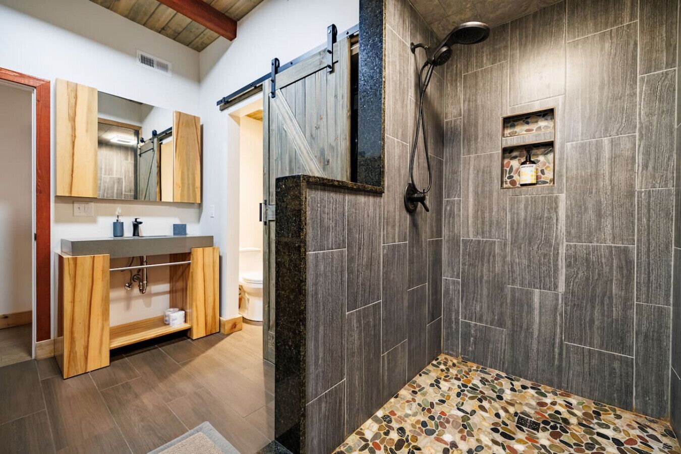 A bathroom with a shower, a wooden vanity, and a mirror.