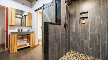 A bathroom with a shower, a wooden vanity, and a mirror.