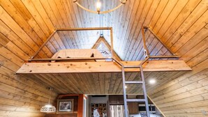 A wooden interior with a loft bedroom, a chandelier, and a ladder. - Canyon A-Frame Cabin | Fire Pit, Sauna, Hiking (Fort Payne)