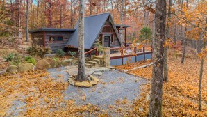 A log cabin with a metal roof, surrounded by a forest with autumn foliage. - Canyon A-Frame Cabin | Fire Pit, Sauna, Hiking (Fort Payne)