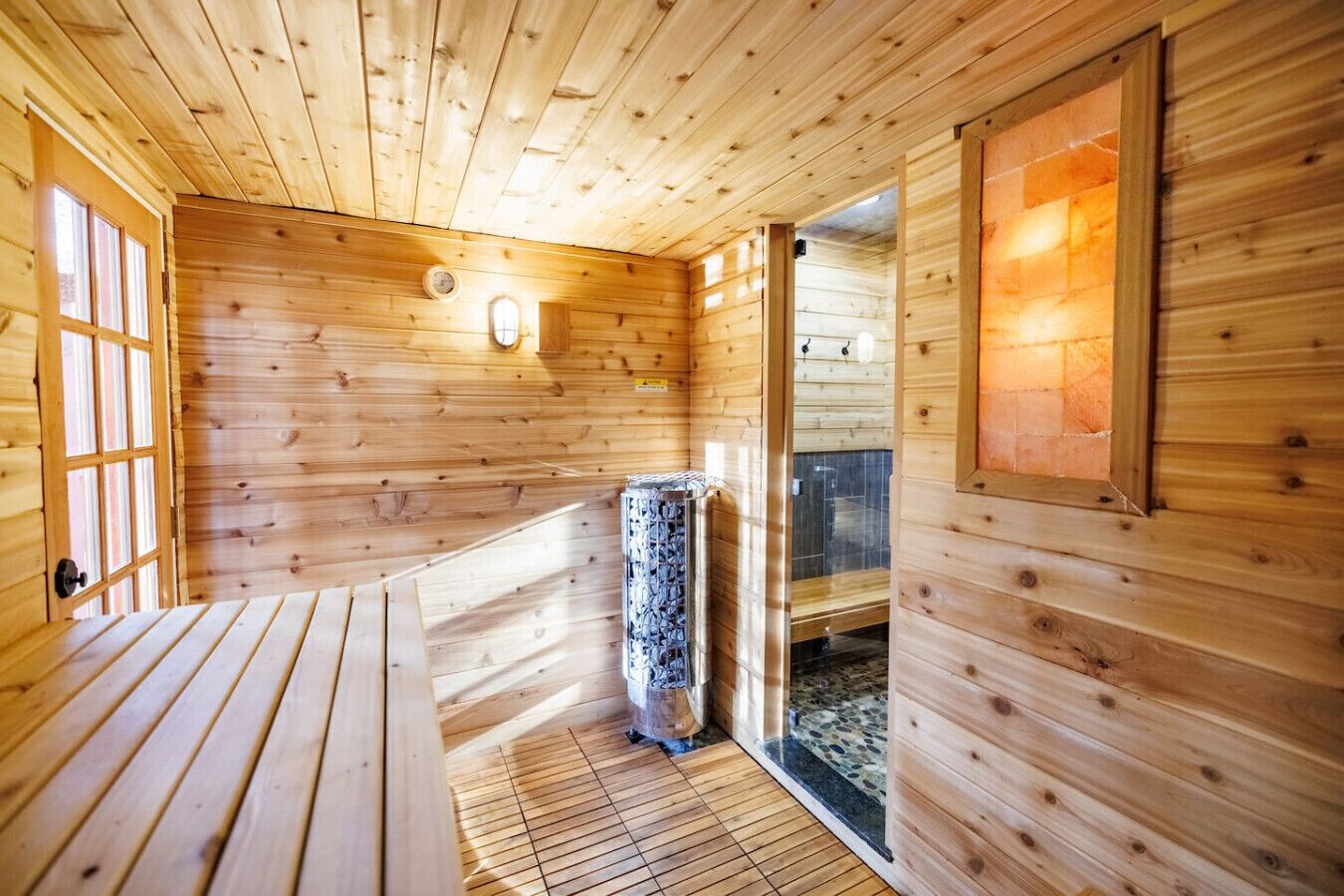 A wooden sauna room with a bench, a glass door leading outside, and a stone floor.