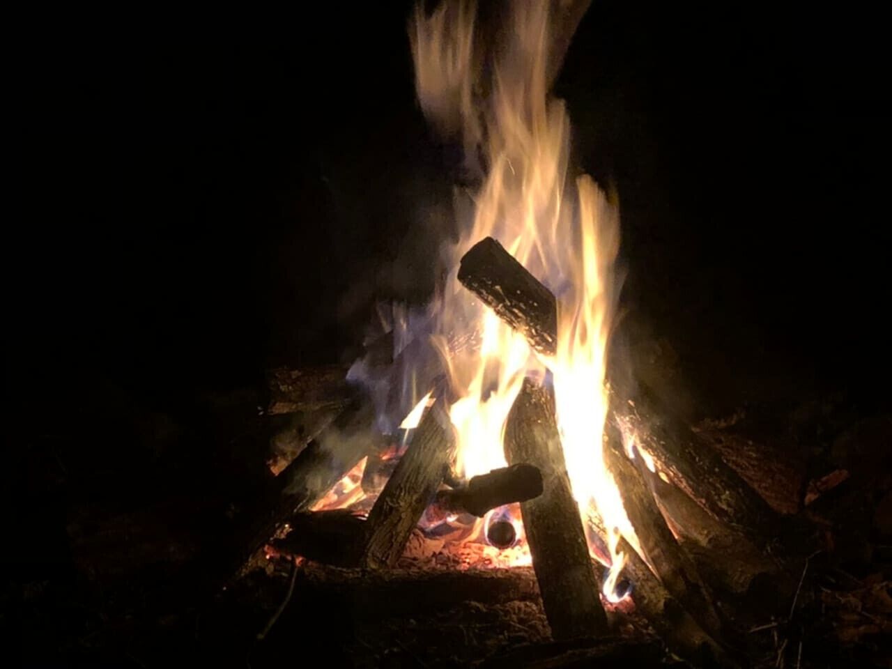 A campfire with logs and a piece of wood burning.