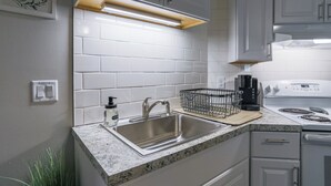 A modern kitchen with white cabinets, a stainless steel sink, a built-in oven, and a granite countertop. - Jelinek Hideaway Unit 1 - Modern 2BR Apartment (Wasusau)