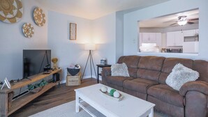 A living room with a brown leather sofa, a white coffee table, a TV on a wooden stand, and a lamp. - Jelinek Hideaway Unit 1 - Modern 2BR Apartment (Wasusau)