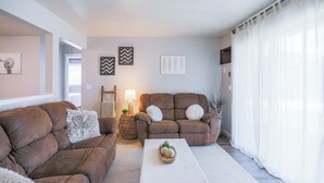 A living room with two brown sofas, a white coffee table, and a lamp. There are decorative wall art pieces and a window with sheer curtains. - Jelinek Hideaway Unit 1 - Modern 2BR Apartment (Wasusau)