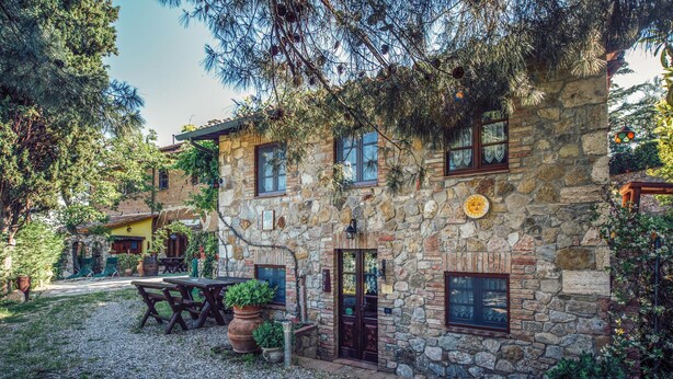 A stone building with a rustic exterior, a wooden door, and a small garden area with a table and chairs. - Lovely apartment in Castiglione d'Orcia (Castiglione d'Orcia)