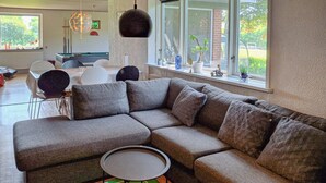Un salon moderne avec un canapé d’angle, une petite table ronde et une vue sur l’extérieur grâce à de grandes fenêtres.