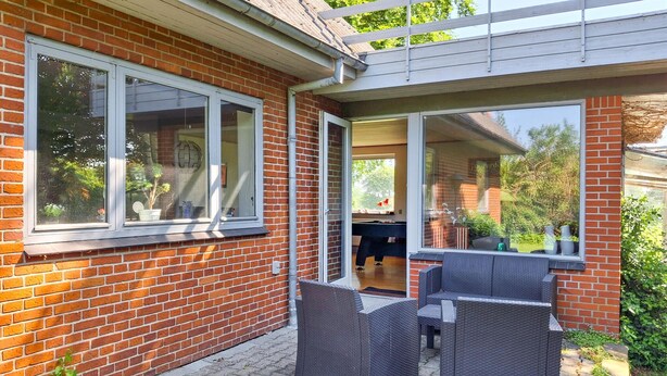 Une maison en briques dotée d’un patio aménagé avec des meubles en osier et offrant une vue sur le jardin arrière.