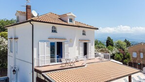 Una casa a due piani con un balcone, pareti bianche e tetto in tegole.