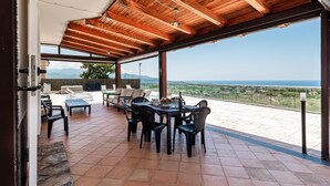 Una veranda riparata con tavolo e sedie, vista sul mare e paesaggio montuoso.