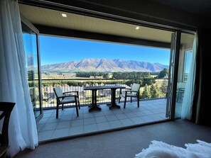 A balcony with a table and chairs, offering a view of mountains and a valley.