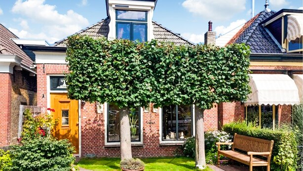 A house with a brick exterior, a wooden door, and a window. There is a bench and a potted plant in the yard. - Lovely home in Sneek with WiFi (Sneek)