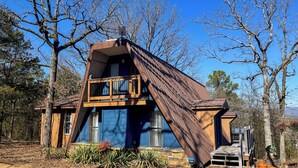 A unique, triangular-shaped cabin with a wooden deck and large windows, surrounded by trees. - Cozy Wister Ridge A-Frame Lake Cabin • Sleeps 6 • Mins to Wister Lake! (Wister)
