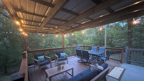 A covered outdoor deck with a dining table and chairs, a sofa, and string lights. - Cozy Wister Ridge A-Frame Lake Cabin • Sleeps 6 • Mins to Wister Lake! (Wister)
