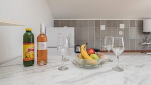 Un comptoir de cuisine avec une bouteille de POG, une bouteille de vin rosé, deux verres à vin et un bol de fruits.