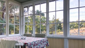 A conservatory with a table set for two, large windows, and a view of trees and hills.