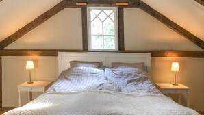 A bedroom with a vaulted ceiling, a large window, two bedside tables with lamps, and a bed with a white duvet.