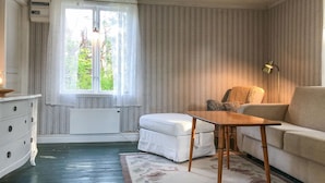 A room with a window, a radiator, a white sofa, a wooden table, and a patterned rug.