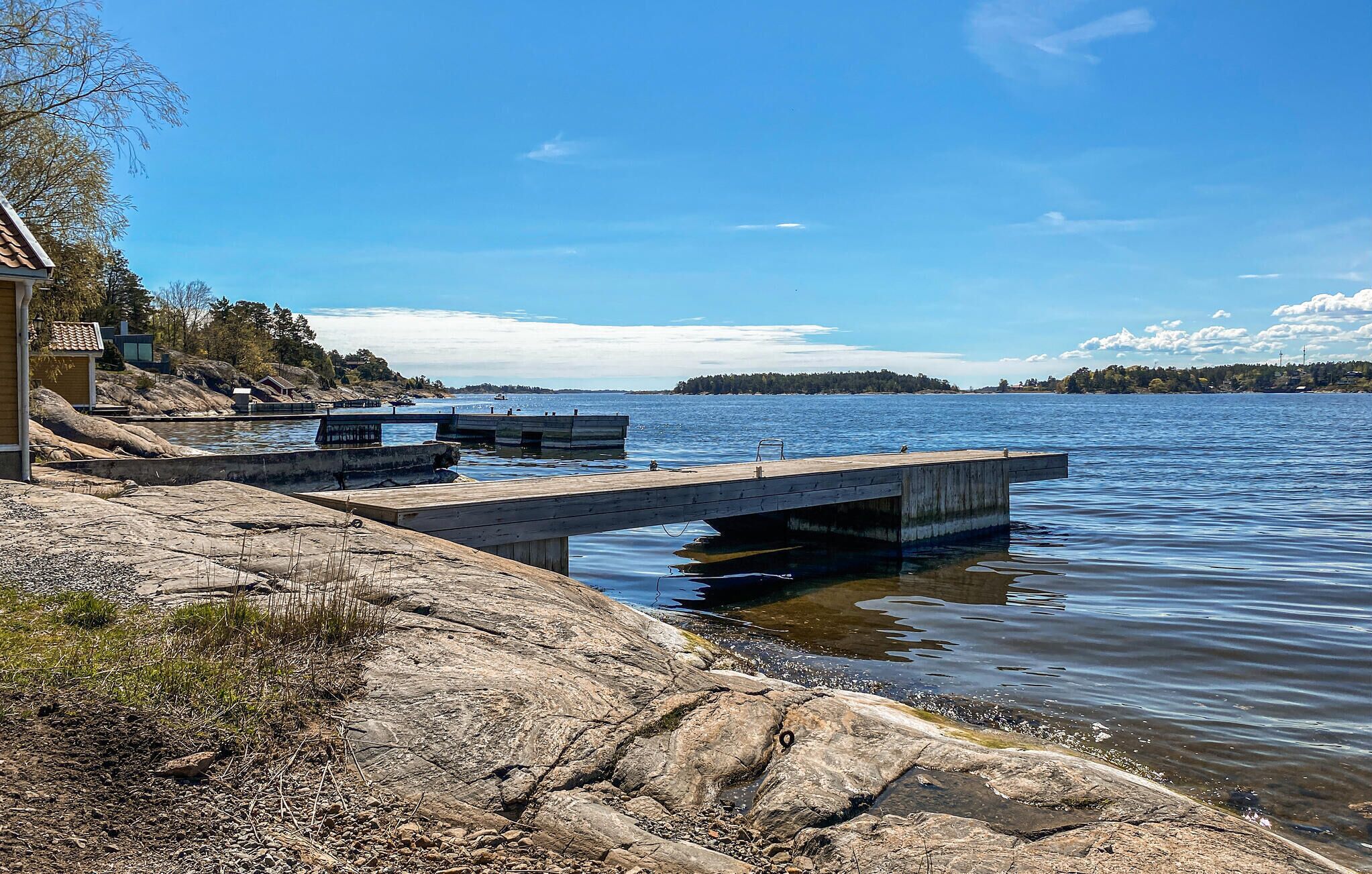 A wooden dock extending into a calm lake, surrounded by rocky terrain and a small building.