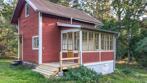 A small, single-story wooden house with a porch and large windows.
