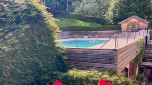 Une terrasse en bois avec une piscine, entourée d’une végétation luxuriante et de fleurs rouges.
