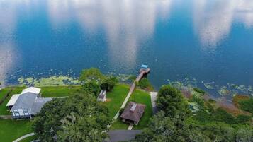 An aerial view of a residential area with a dock extending into a lake, surrounded by lush greenery and houses.