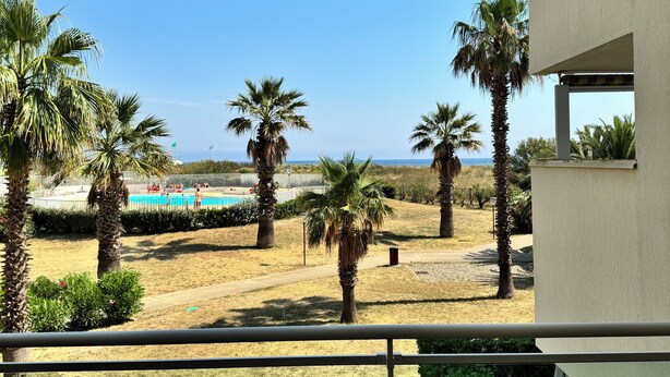 Un balcón con vistas a una piscina, palmeras y un cielo despejado.