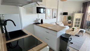 Una cocina moderna con estufa integrada, microondas y lavaplatos. Cuenta con una zona de comedor con mesa y sillas, y una pequeña planta en el alféizar.
