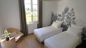 Een slaapkamer met twee bedden, een raam met gordijnen, een rieten stoel en een plant in een pot.