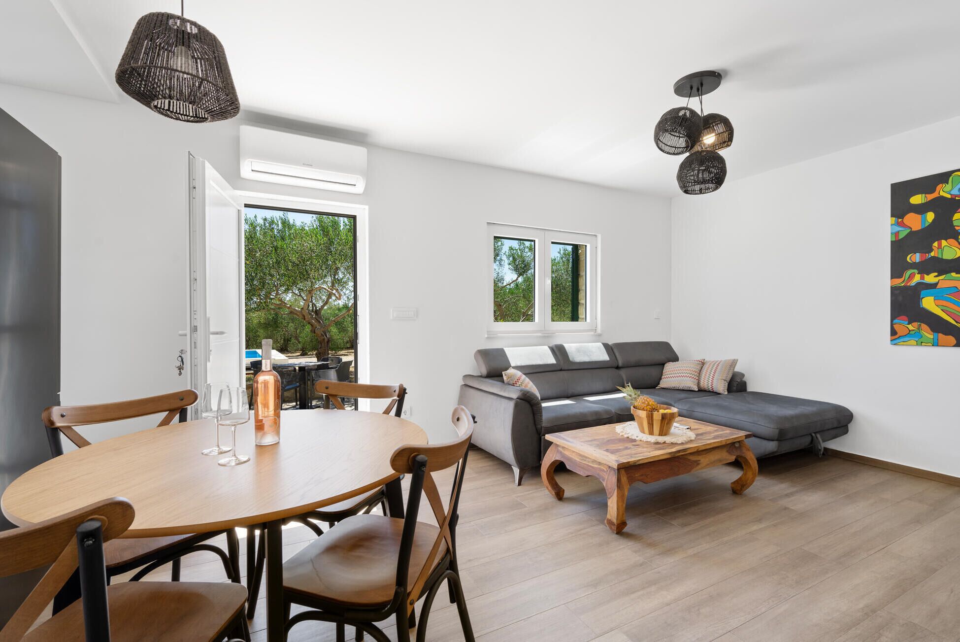 A modern living room with a grey sofa, wooden coffee table, and a dining area with a round table and chairs.