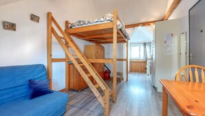 Una habitación compacta con una cama litera, un sofá azul, una mesa de madera y una zona de cocina.
