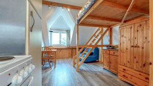 Interior acogedor de una cabaña con cocina, comedor y habitación superior con escalera de madera.
