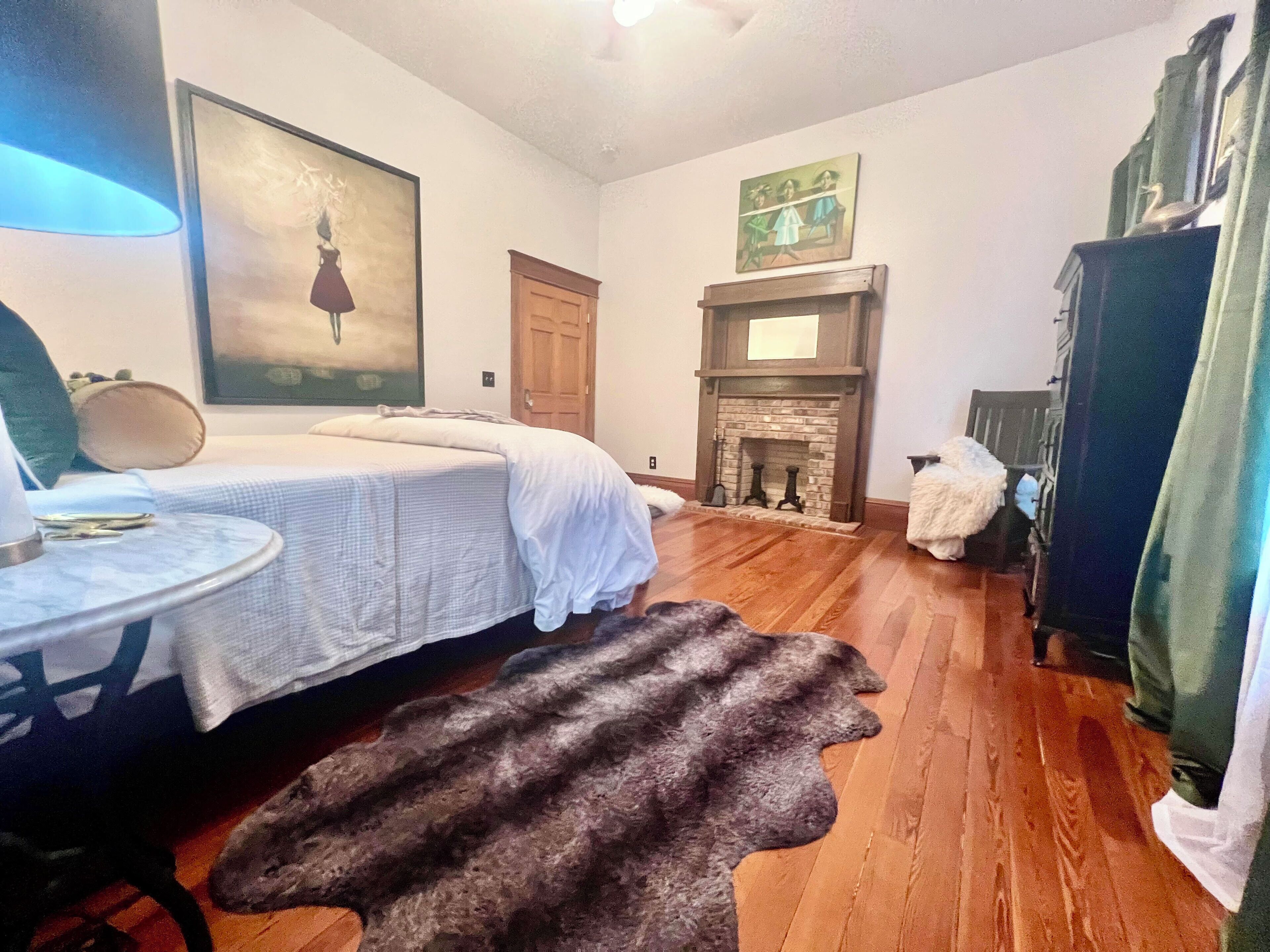 A room with a bed, a fireplace, a fur rug, and a table with a lamp.