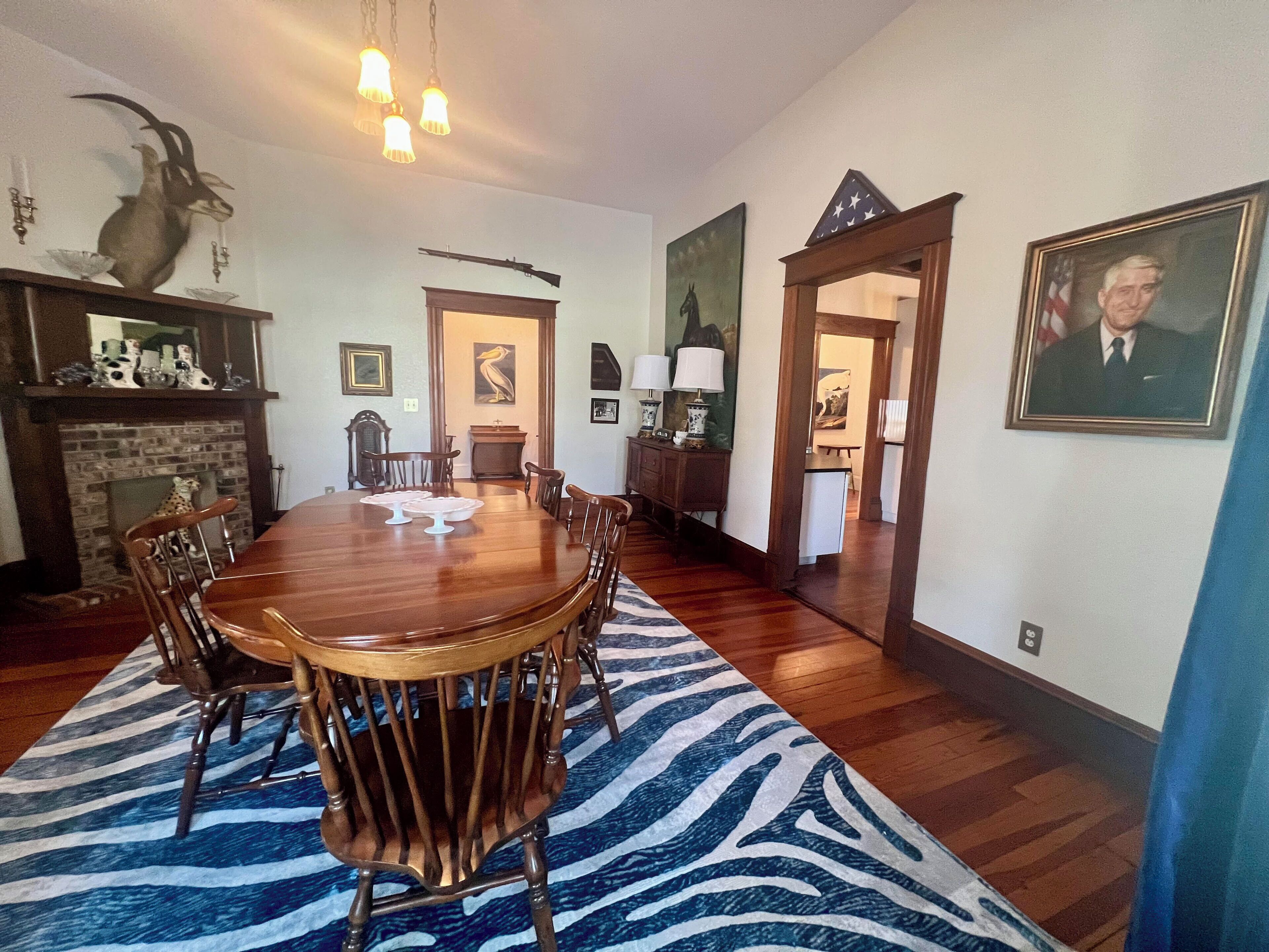 A dining room with a large wooden table surrounded by chairs, a zebra-patterned rug, and a fireplace.