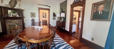 A dining room with a large wooden table surrounded by chairs, a zebra-patterned rug, and a fireplace.