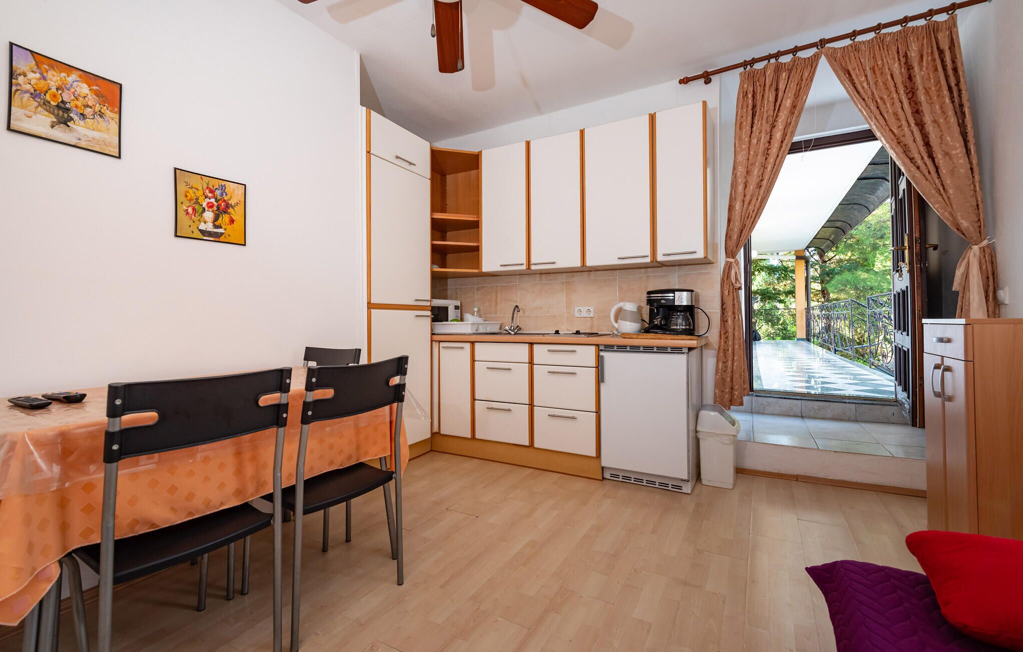 A compact kitchen with white cabinets, a dining table with chairs, and a view of a balcony with a railing.
